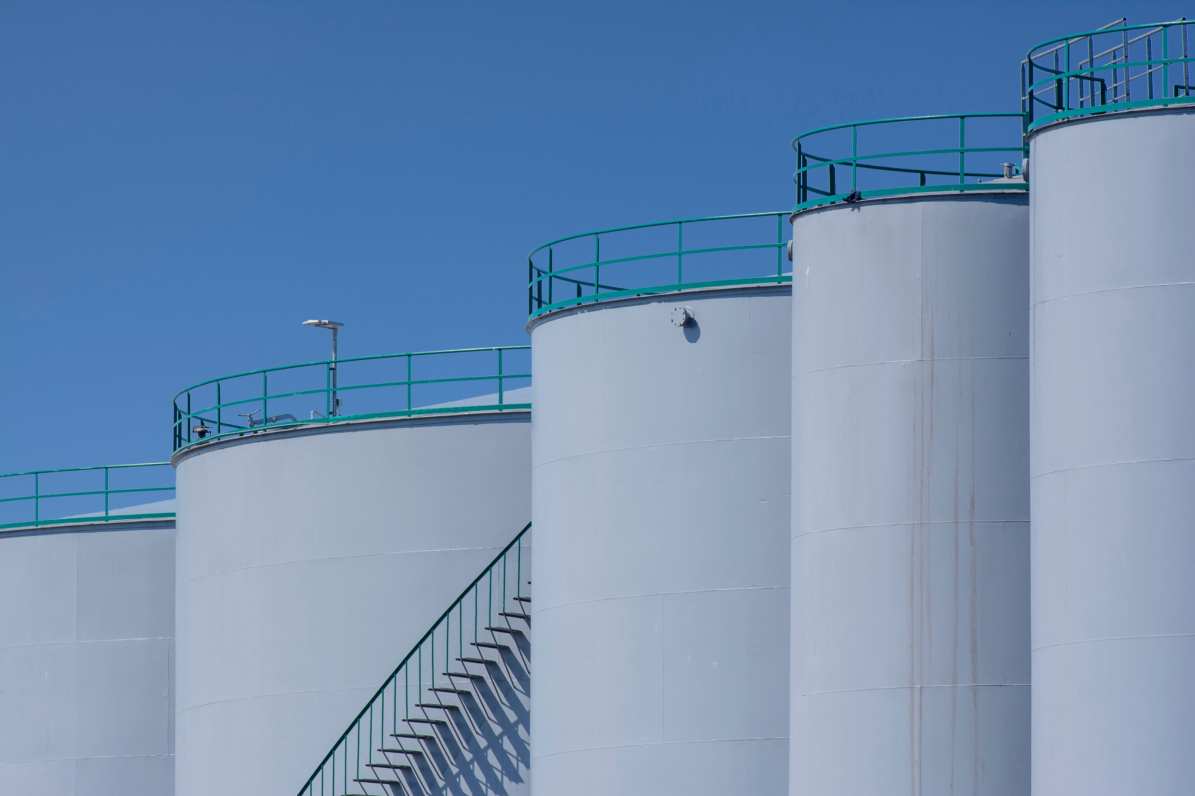 Stora industriella lagringstankar med gröna räcken mot en klarblå himmel