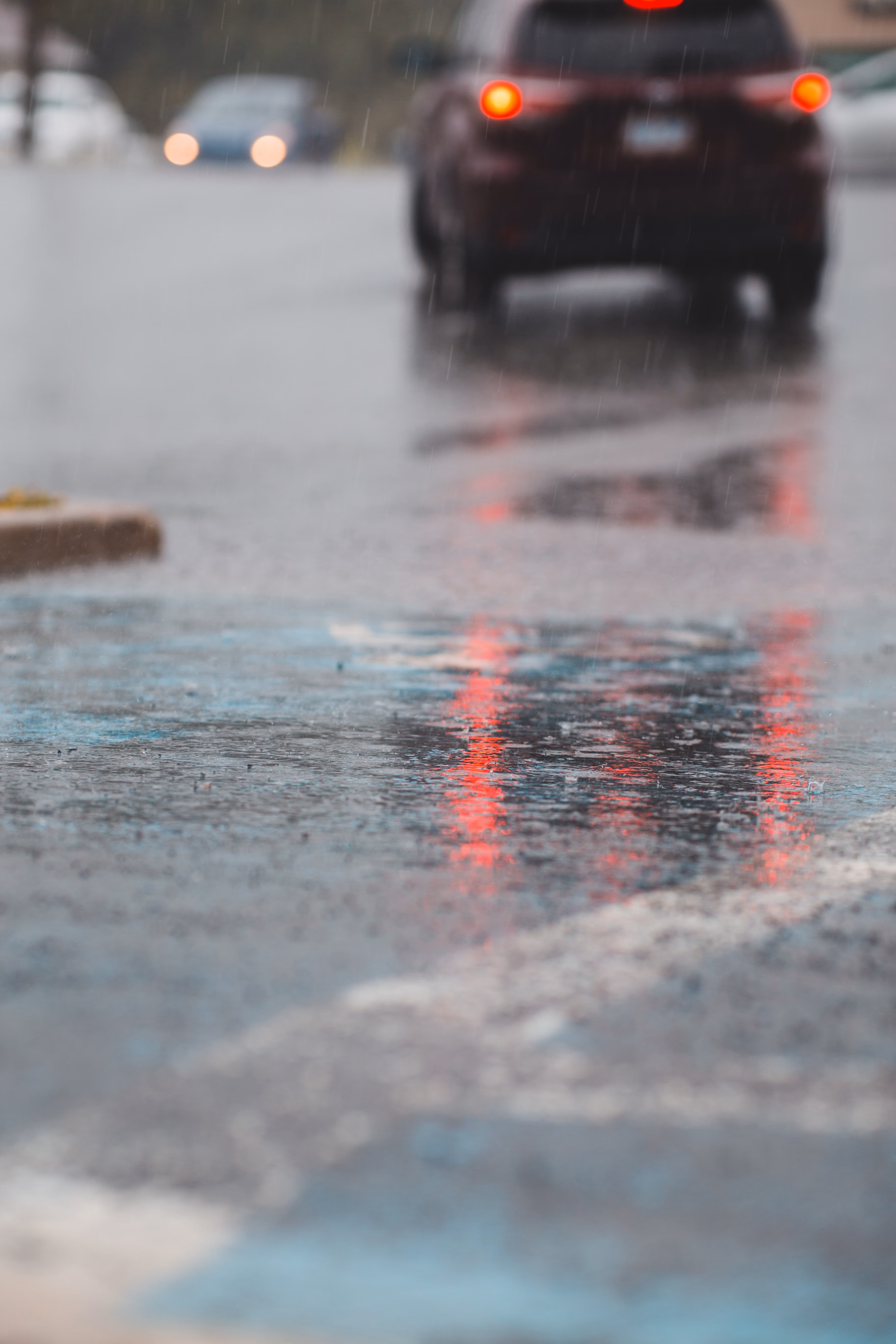 Bilar med tända lyktor på en blöt asfaltväg i regn, sedd i marknivå